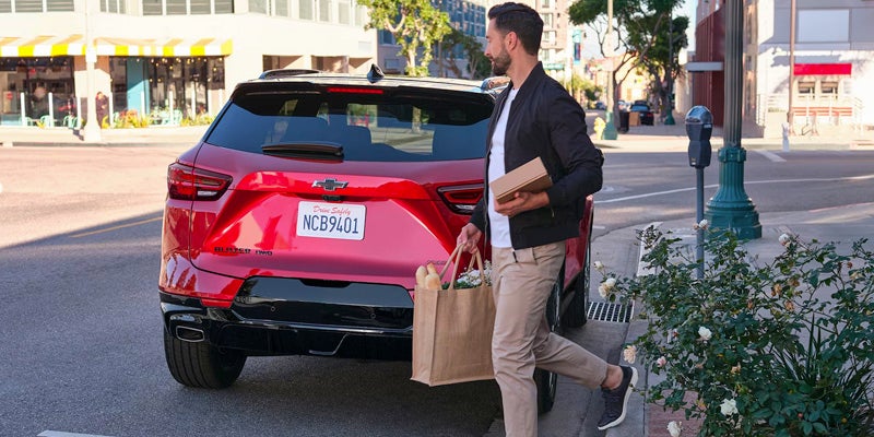 Man with groceries approaching the back of a red Chevrolet Blazer.