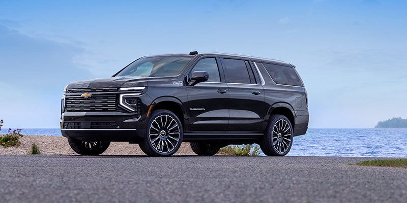 Dark gray Chevrolet Suburban parked on pavement near a lake or ocean