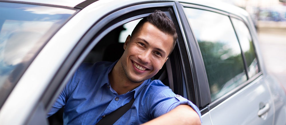Smiling man sitting in a car, looking out the window.