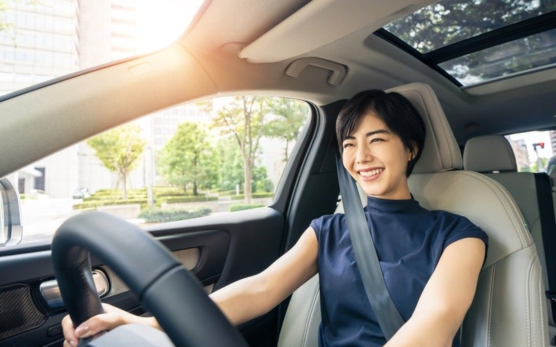 Smiling girl driving a car with sunlight shining through the window.