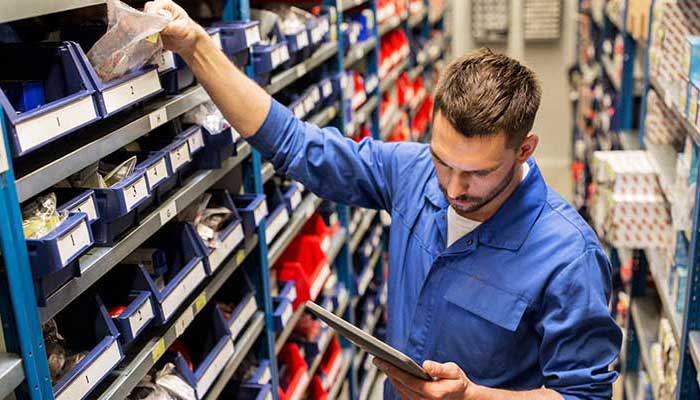 Numerous small car parts are placed in different compartments and technician is picking parts as per the list in his hand.